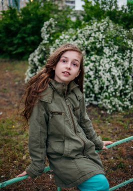 Sokaktaki küçük kız yeşil yapraklı bir arka plana karşı. Uzun saçlı kız. Çocuk 9-10 yaşlarında..