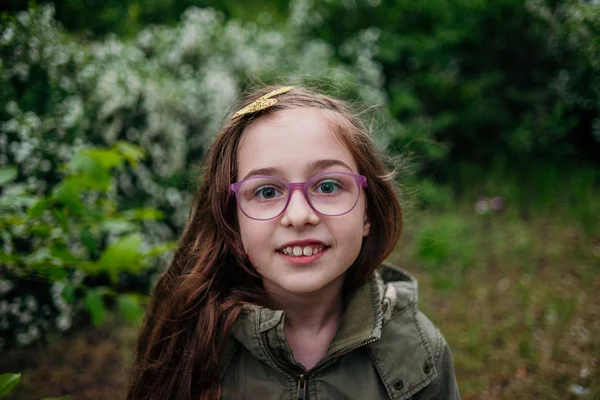 Маленькая девочка на улице на фоне зеленой листвы. Девушка с длинными волосами. Ребенок 9-10 лет . — стоковое фото