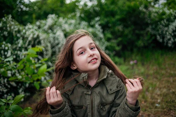 Little girl on the street against a background of green foliage. Girl with long hair. Child 9-10 years old girl. — ストック写真