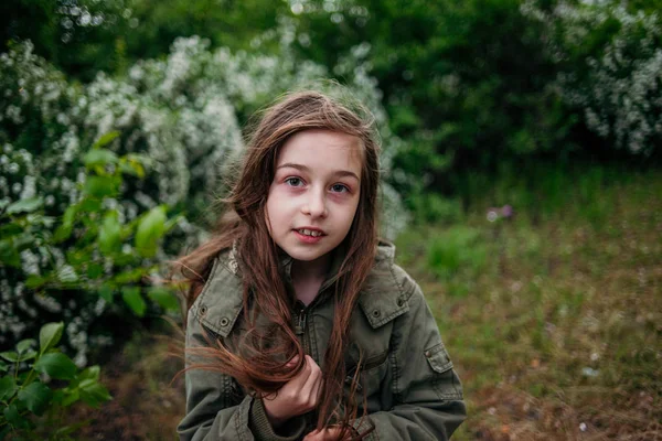 Holčička na ulici na pozadí zeleného listí. Dívka s dlouhými vlasy. Dítě 9-10 let dívka. — Stock fotografie