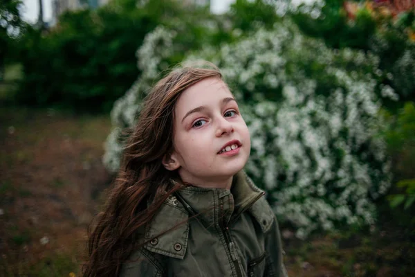 Liten flicka på gatan mot en bakgrund av grönt lövverk. Flicka med långt hår. Barn 9-10 år gammal flicka. — Stockfoto