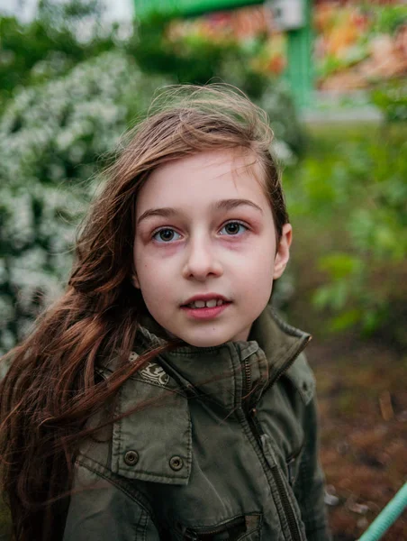 Klein meisje op straat tegen een achtergrond van groen gebladerte. Meisje met lang haar. Kind 9-10 jaar oud meisje. — Stockfoto