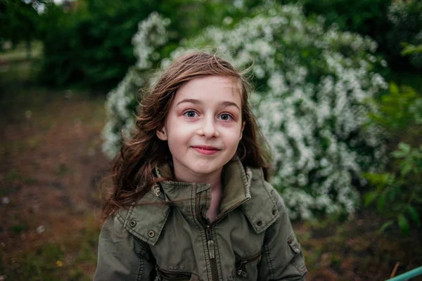 Klein meisje op straat tegen een achtergrond van groen gebladerte. Meisje met lang haar. Kind 9-10 jaar oud meisje. — Stockfoto