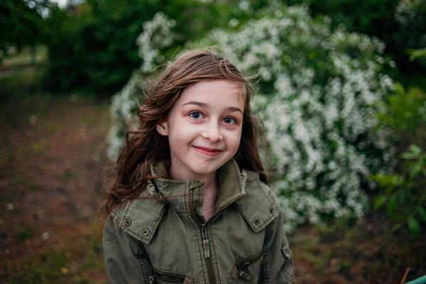Egy kislány az utcán, zöld lombozat hátterében. Hosszú hajú lány. 9-10 éves kislány. — Stock Fotó