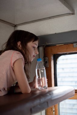 Eski bir trenle gezen bir kız. Yakınlarda bir şişe su var..