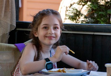 Çocuk yemek yiyor. Küçük kız patates kızartması yiyor. 9 yıllık kızlar. Sokakta açık bir kafe..