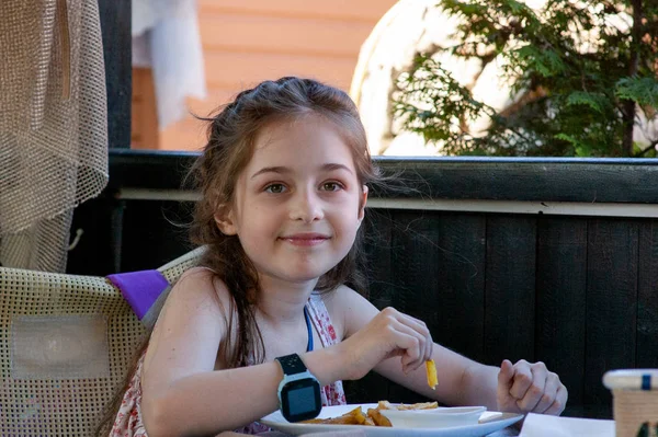 Das Kind isst. kleines Mädchen isst Pommes. Mädchen von 9 Jahren. Café im Freien auf der Straße. — Stockfoto