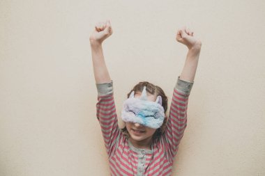 Yüzünde yumuşak, beyaz, uykulu tek boynuzlu at olan düz saçlı bir kız. Tek boynuzlu at maskeli kız. 9 yaşında..