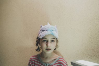 Yüzünde yumuşak, beyaz, uykulu tek boynuzlu at olan düz saçlı bir kız. Tek boynuzlu at maskeli kız. 9 yaşında..