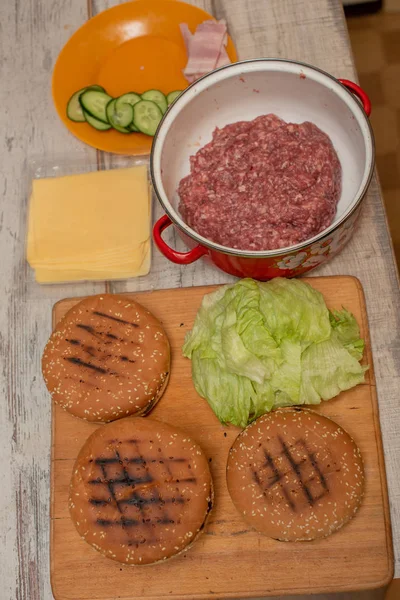 Hamburgers bakken, een hamburger maken, foto 's maken met broodjes, rauw vlees, kaas en groenten op tafel. — Stockfoto