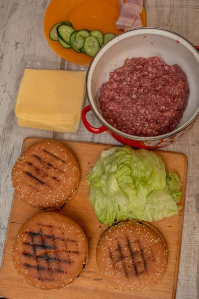 Hamburgers bakken, een hamburger maken, foto 's maken met broodjes, rauw vlees, kaas en groenten op tafel. — Stockfoto