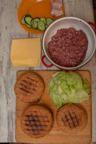 Cozinhando hambúrgueres, fazendo um hambúrguer, imagens com pães, carne crua, queijo e legumes na mesa . — Fotografia de Stock