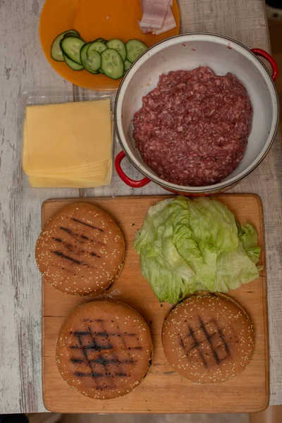 Cozinhando hambúrgueres, fazendo um hambúrguer, imagens com pães, carne crua, queijo e legumes na mesa . — Fotografia de Stock