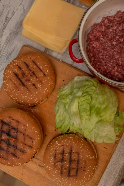 Cottura hamburger, fare un hamburger, immagini con panini, carne cruda, formaggio e verdure sulla tavola . — Foto Stock