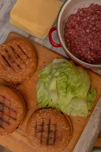 Cottura hamburger, fare un hamburger, immagini con panini, carne cruda, formaggio e verdure sulla tavola . — Foto Stock