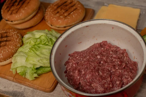 Cozinhando hambúrgueres, fazendo um hambúrguer, imagens com pães, carne crua, queijo e legumes na mesa . — Fotografia de Stock