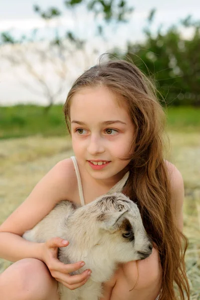 Menina com cabra bebê na fazenda ao ar livre. Animais de aldeia. criança feliz abraços cabra, conceito de unidade da natureza e do homem . — Fotografia de Stock