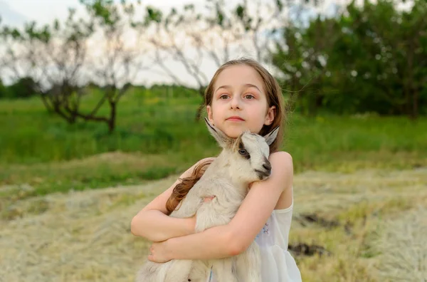 Menina com cabra bebê na fazenda ao ar livre. Animais de aldeia. criança feliz abraços cabra, conceito de unidade da natureza e do homem . — Fotografia de Stock