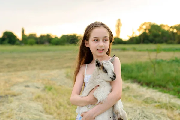 Девочка с козленком на ферме на открытом воздухе. Деревенские животные. счастливый ребенок обнимает козу, понятие единства природы и человека . — стоковое фото