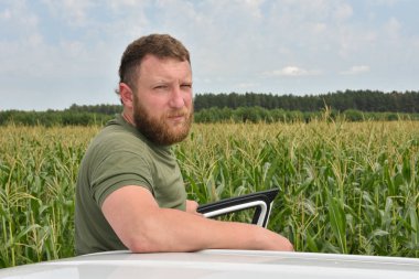 Yazın mısır tarlasının yakınındaki çiftçi. Tarlanın arka planında mısır arabalı beyaz bir adam.