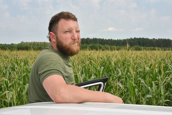 Fermier lângă câmpul de porumb în timpul verii. Un om pe fundalul unui câmp cu o mașină de porumb albă — Fotografie, imagine de stoc