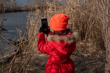 Sevimli kız, kırmızı ceketli, fotoğraf çekmek için poz veriyor ya da akıllı telefonuyla kendi fotoğrafını çekiyor.