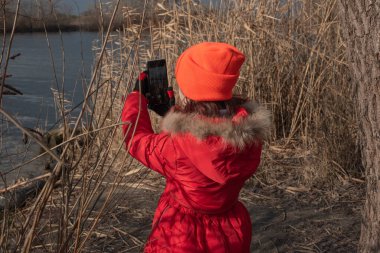 Sevimli kız, kırmızı ceketli, fotoğraf çekmek için poz veriyor ya da akıllı telefonuyla kendi fotoğrafını çekiyor.