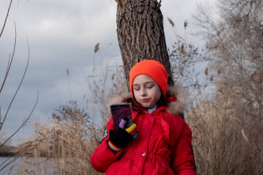 Sevimli kız, kırmızı ceketli, fotoğraf çekmek için poz veriyor ya da akıllı telefonuyla kendi fotoğrafını çekiyor.