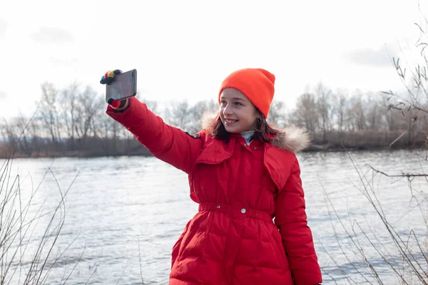 Adorable Chica, vestida con chaqueta roja, posa para hacer selfie o foto de sí misma con teléfono inteligente — Foto de Stock