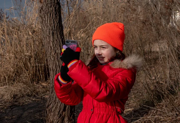 Adorabile ragazza, vestita in giacca rossa, posa per fare selfie o foto di se stessa con lo smartphone — Foto Stock