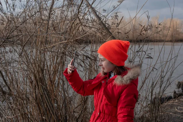 Adorable Chica, vestida con chaqueta roja, posa para hacer selfie o foto de sí misma con teléfono inteligente — Foto de Stock