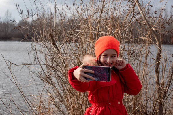 Adorável menina, vestida com jaqueta vermelha, posa para fazer selfie ou foto de si mesma com smartphone — Fotografia de Stock