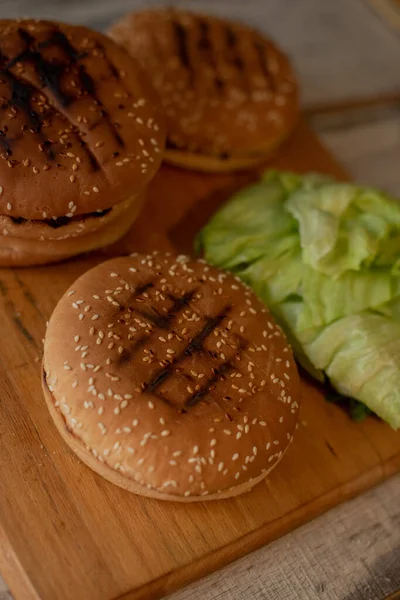 Hamburgers bakken, een hamburger maken, foto 's met broodjes, groenten op tafel. broodjes en gehakt voor het maken van hamburgers. IJsbergsla bladeren. — Stockfoto