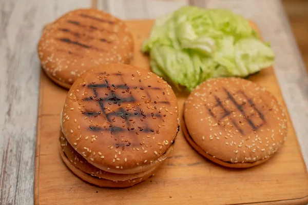 Cozinhando hambúrgueres, fazendo um hambúrguer, fotos com pães, legumes na mesa. rolos e carne picada para fazer hambúrgueres. Folhas de alface-de-iceberg . — Fotografia de Stock