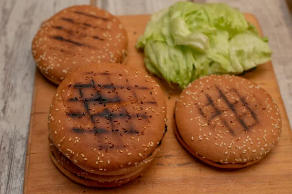 Cottura hamburger, fare un hamburger, immagini con panini, verdure sul tavolo. rotoli e carne macinata per fare hamburger. Foglie di lattuga iceberg . — Foto Stock