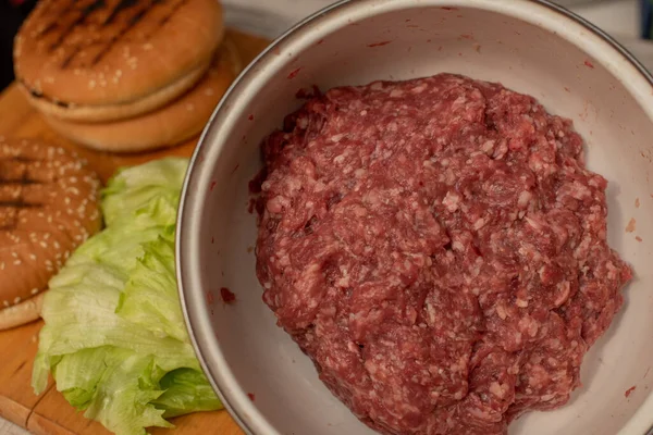 Hamburger kochen, Hamburger zubereiten, Bilder mit Brötchen, rohem Fleisch und Gemüse auf dem Tisch. — Stockfoto