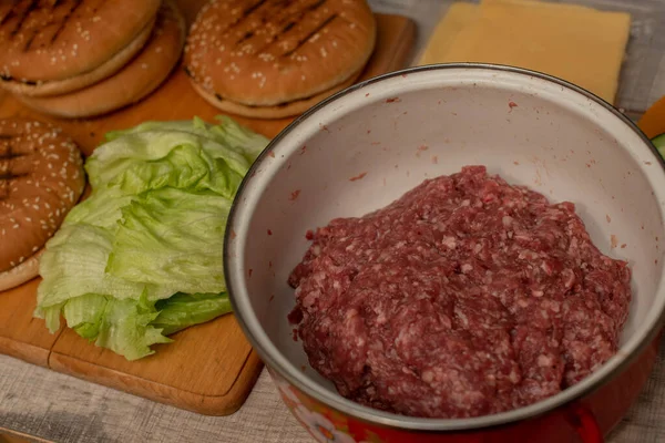 Cottura hamburger, fare un hamburger, immagini con panini, carne cruda, e verdure sulla tavola . — Foto Stock