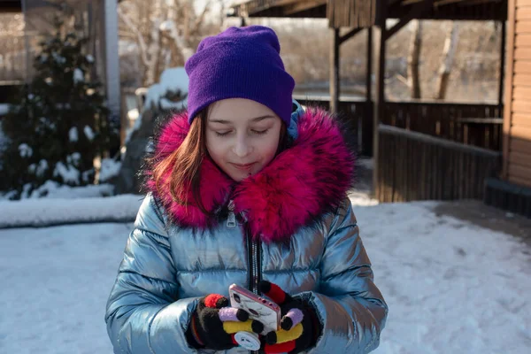 Uśmiechnięta kobieta z telefonem komórkowym chodząca po ulicy. Dziewczyna 9 lat na ulicy w zimie trzymając telefon — Zdjęcie stockowe