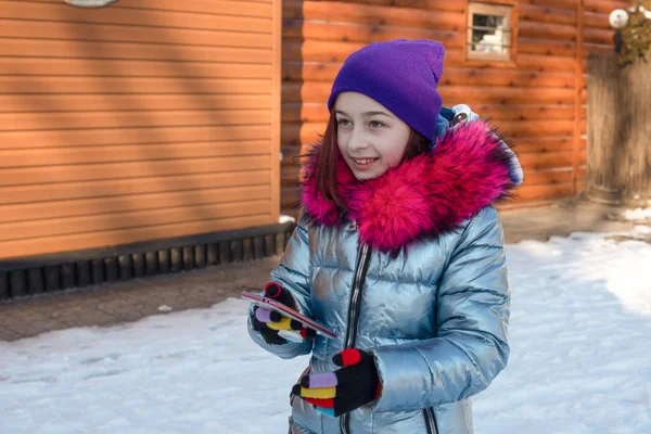 Uśmiechnięta kobieta z telefonem komórkowym chodząca po ulicy. Dziewczyna 9 lat na ulicy w zimie trzymając telefon — Zdjęcie stockowe