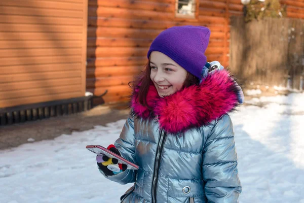 Femme souriante avec téléphone portable marchant dans la rue. Fille 9 ans dans la rue en hiver tenant un téléphone — Photo