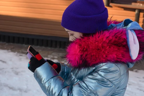 Donna sorridente con cellulare che cammina per strada. Ragazza di 9 anni per strada in inverno con un telefono in mano — Foto Stock