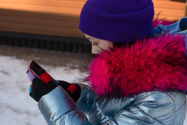 Donna sorridente con cellulare che cammina per strada. Ragazza di 9 anni per strada in inverno con un telefono in mano — Foto Stock