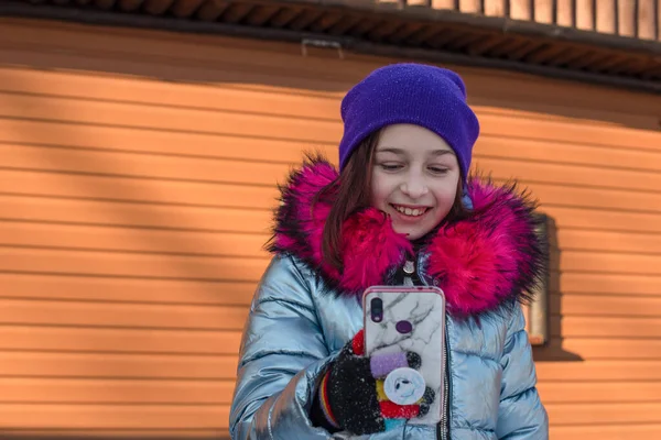 Mulher sorridente com telefone celular andando na rua. Menina 9 anos de idade na rua no inverno segurando um telefone — Fotografia de Stock