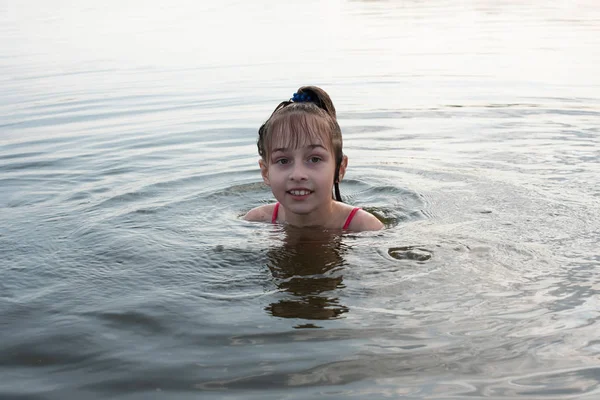 Удовольствие красивая маленькая девочка плавает в голубой воде, наклоняется из воды и улыбается. Девочка-подросток наслаждается теплой погодой — стоковое фото