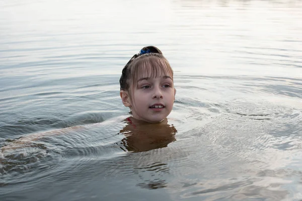 Удовольствие красивая маленькая девочка плавает в голубой воде, наклоняется из воды и улыбается. Девочка-подросток наслаждается теплой погодой — стоковое фото