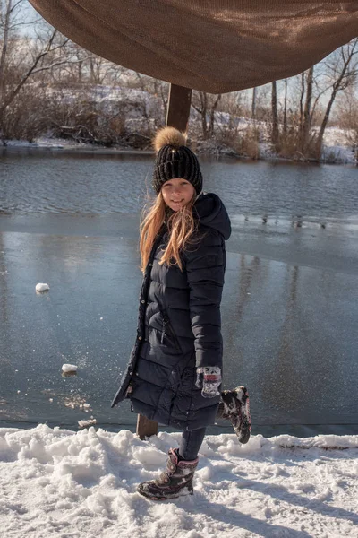 girl on the background of winter lake or river. landscape with frozen lake. winter season. Girl in winter clothes on a background of the river. Girl 9 years old against the background of a small river