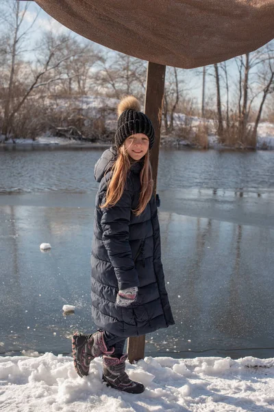 girl on the background of winter lake or river. landscape with frozen lake. winter season. Girl in winter clothes on a background of the river. Girl 9 years old against the background of a small river