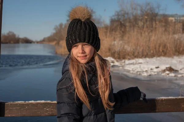 girl on the background of winter lake or river. landscape with frozen lake. winter season. Girl in winter clothes on a background of the river. Girl 9 years old against the background of a small river