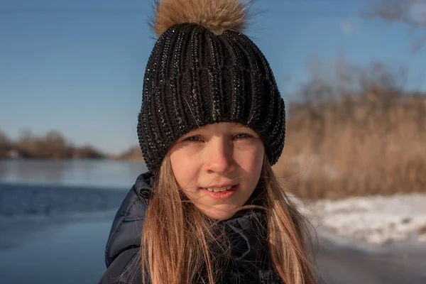 girl on the background of winter lake or river. landscape with frozen lake. winter season. Girl in winter clothes on a background of the river. Girl 9 years old against the background of a small river