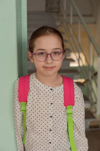 Girl 9 years old with a school backpack on her back. Portrait of a schoolgirl 9 years old. 4th grade school.Schoolgirl at school with a pink backpack. Back to school.9 years old girl in a white blouse